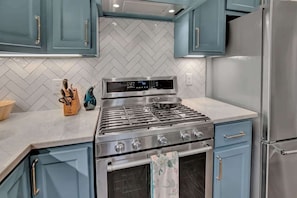 A modern kitchen with a stainless steel stove, blue cabinets, and a white herringbone backsplash. - 500 Feet 2 Main St-Fred Charmer! (Fredericksburg)
