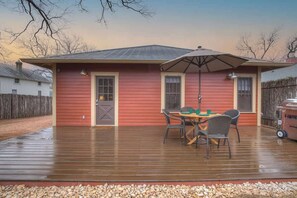 Une maison rouge avec une terrasse en bois, une table avec des chaises et un barbecue.
