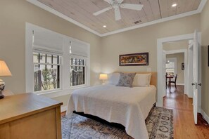 A bedroom with a bed, a desk, a window, and a ceiling fan.