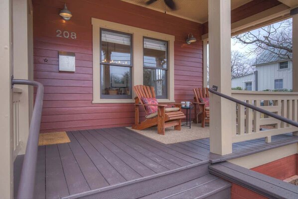 A wooden porch with two chairs and a table, a number '208' on the wall, and a railing.