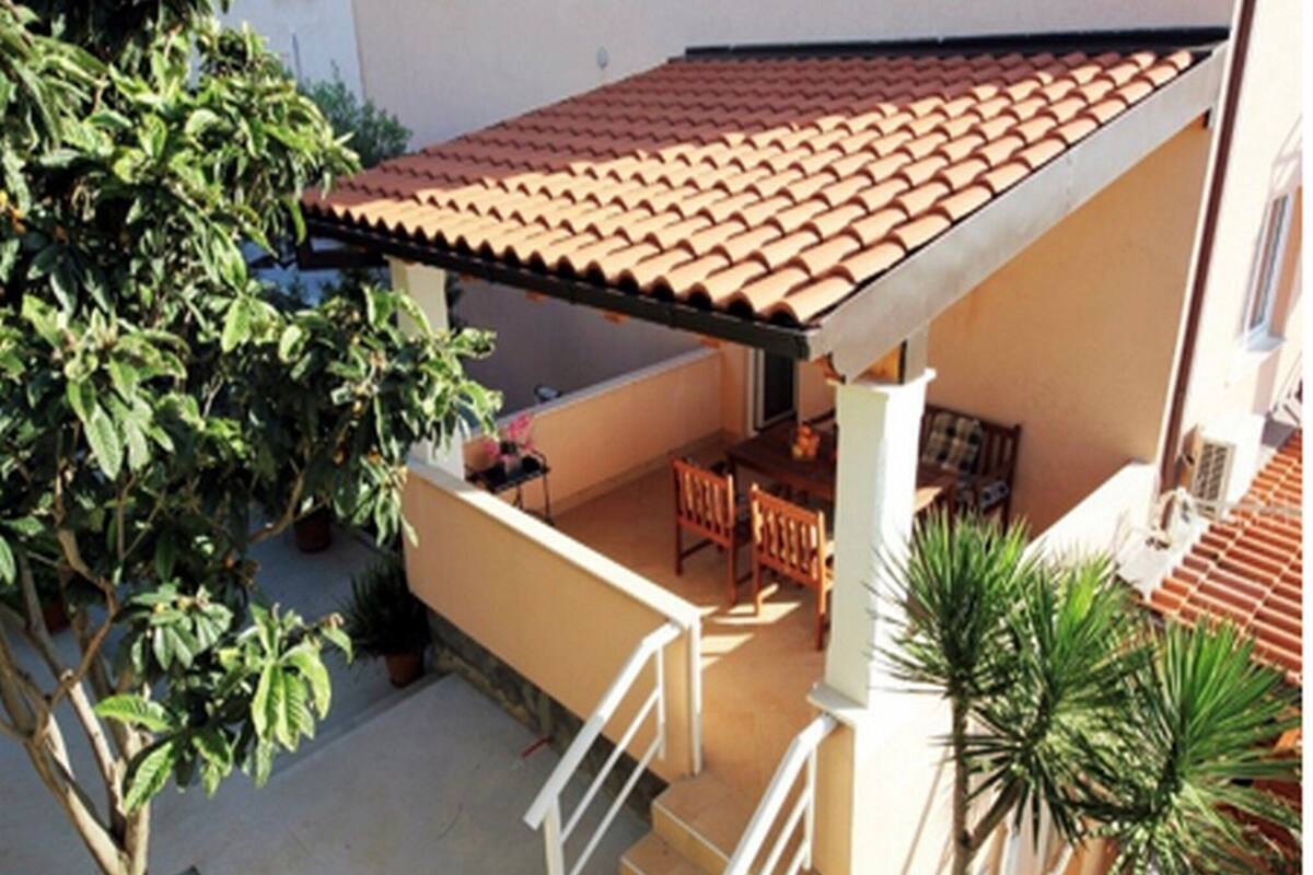 A covered patio with a tiled roof, outdoor furniture, and potted plants.