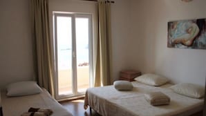 A hotel room with two beds, a sliding glass door to the beach, and a painting on the wall. - Apartments Anita (Konavle)