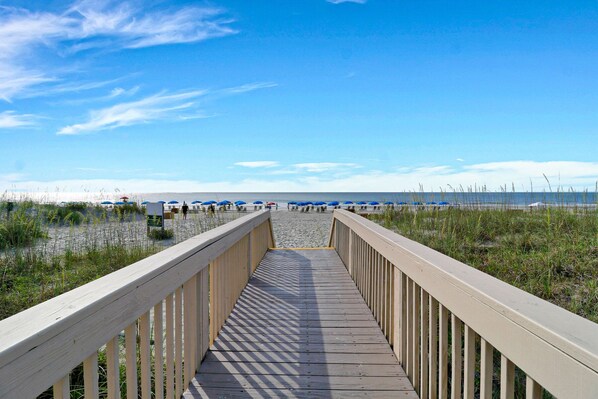 A wooden boardwalk leading to a beach with blue umbrellas.
