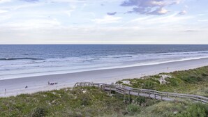 Ein Strand mit einer Holzpromenade, die zum Ufer führt, feinem Sand und dem Ozean.