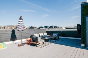 A rooftop deck with outdoor seating, a flagpole, and a view of surrounding buildings.