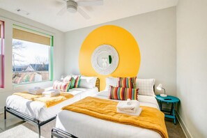 Une chambre d’hôtel moderne avec deux lits, une grande décoration murale circulaire, une fenêtre avec vue et une petite table avec une lampe.