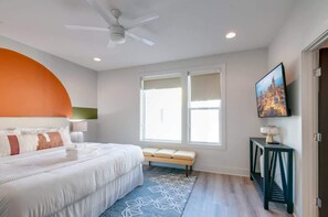 A bedroom with a bed, a bench, a TV, and a ceiling fan.