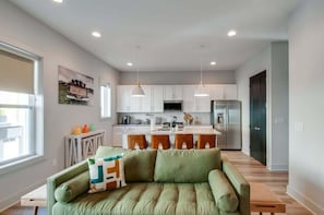 A modern kitchen with white cabinets, a central island with stools, and a dining area with a green sofa and a small table.