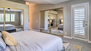 A bedroom with a bed, a ceiling fan, a large mirror, and a door with blinds. - Chic Palm Desert Condo w/ Resort-Style Amenities! (Palm Desert)