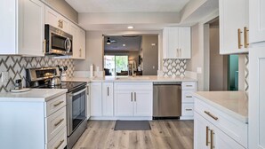 A modern kitchen with white cabinetry, stainless steel appliances, and a herringbone-patterned backsplash. - Chic Palm Desert Condo w/ Resort-Style Amenities! (Palm Desert)