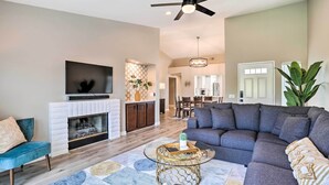 A spacious living room with a sectional sofa, a fireplace, a ceiling fan, and a dining area in the background. - Chic Palm Desert Condo w/ Resort-Style Amenities! (Palm Desert)