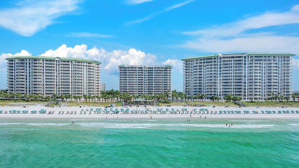 A beachfront hotel with multiple high-rise buildings, a sandy beach, and clear turquoise waters. - Silver Shells St Lucia 501 - Beachfront, Heated Community Pool + Hot Tub! (Destin)