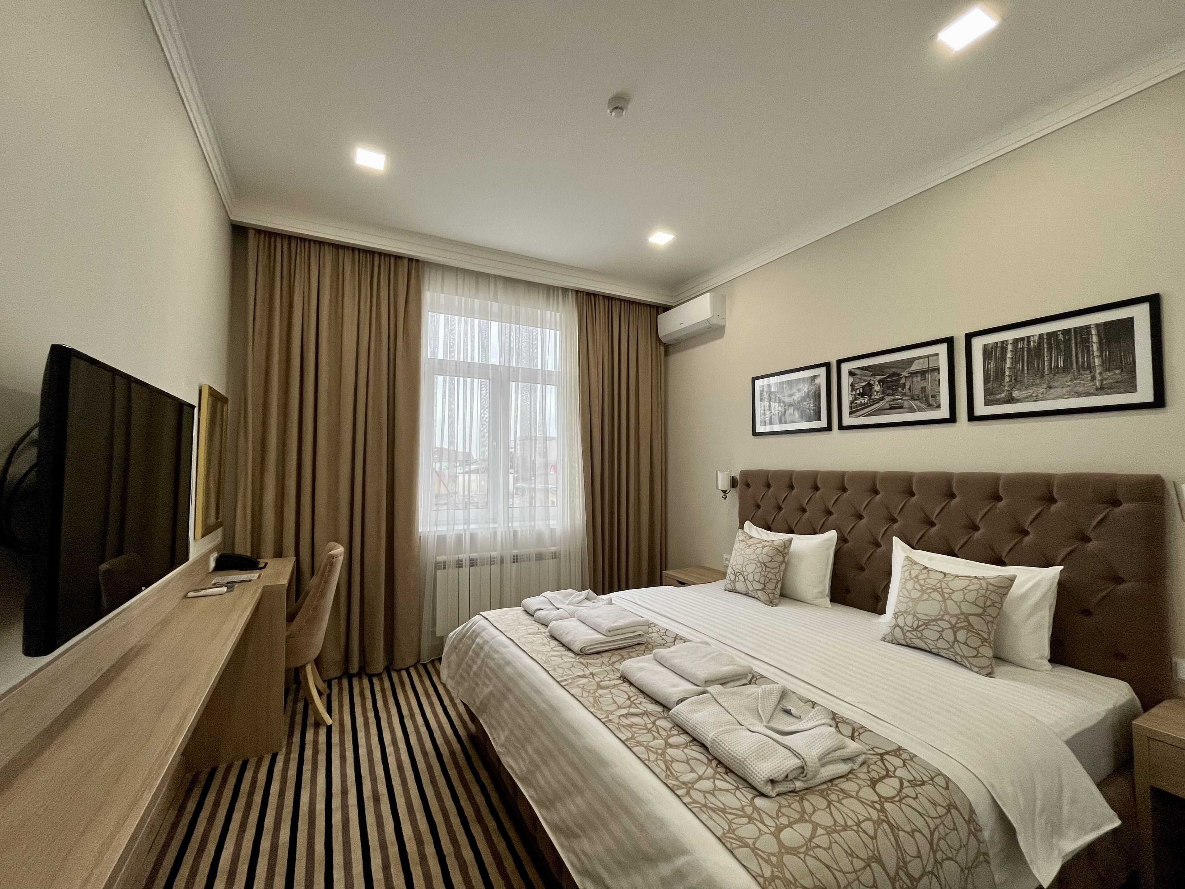Una habitación de hotel con cama, escritorio, televisor y ventana con cortinas.