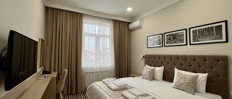 Una habitación de hotel con cama, escritorio, televisor y ventana con cortinas.