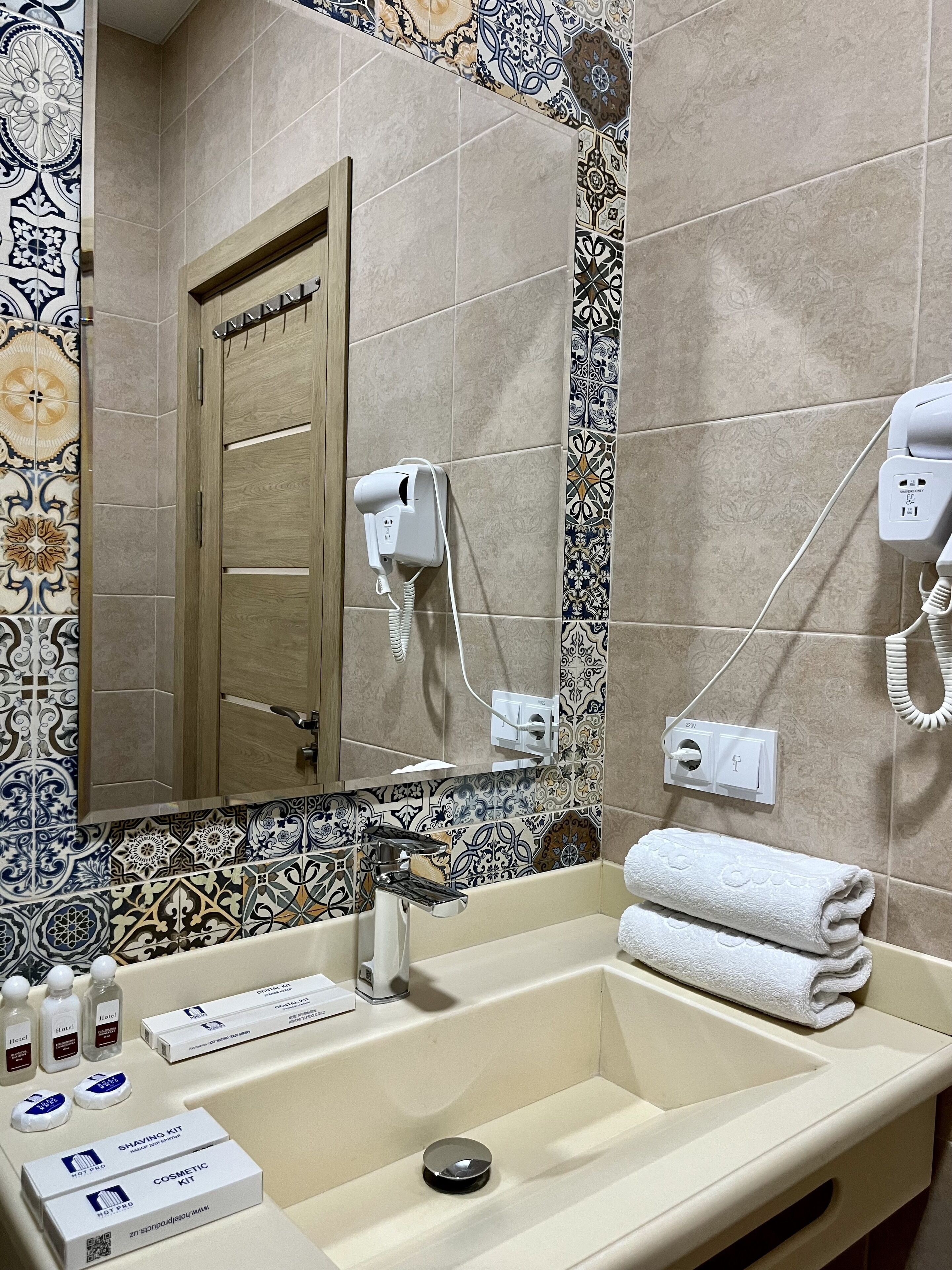 A bathroom with a sink, mirror, and towel rack. There are toiletries and a shaving kit on the counter.