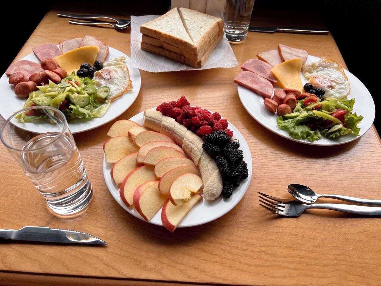 A table with plates of food, including sandwiches, fruits, and vegetables.