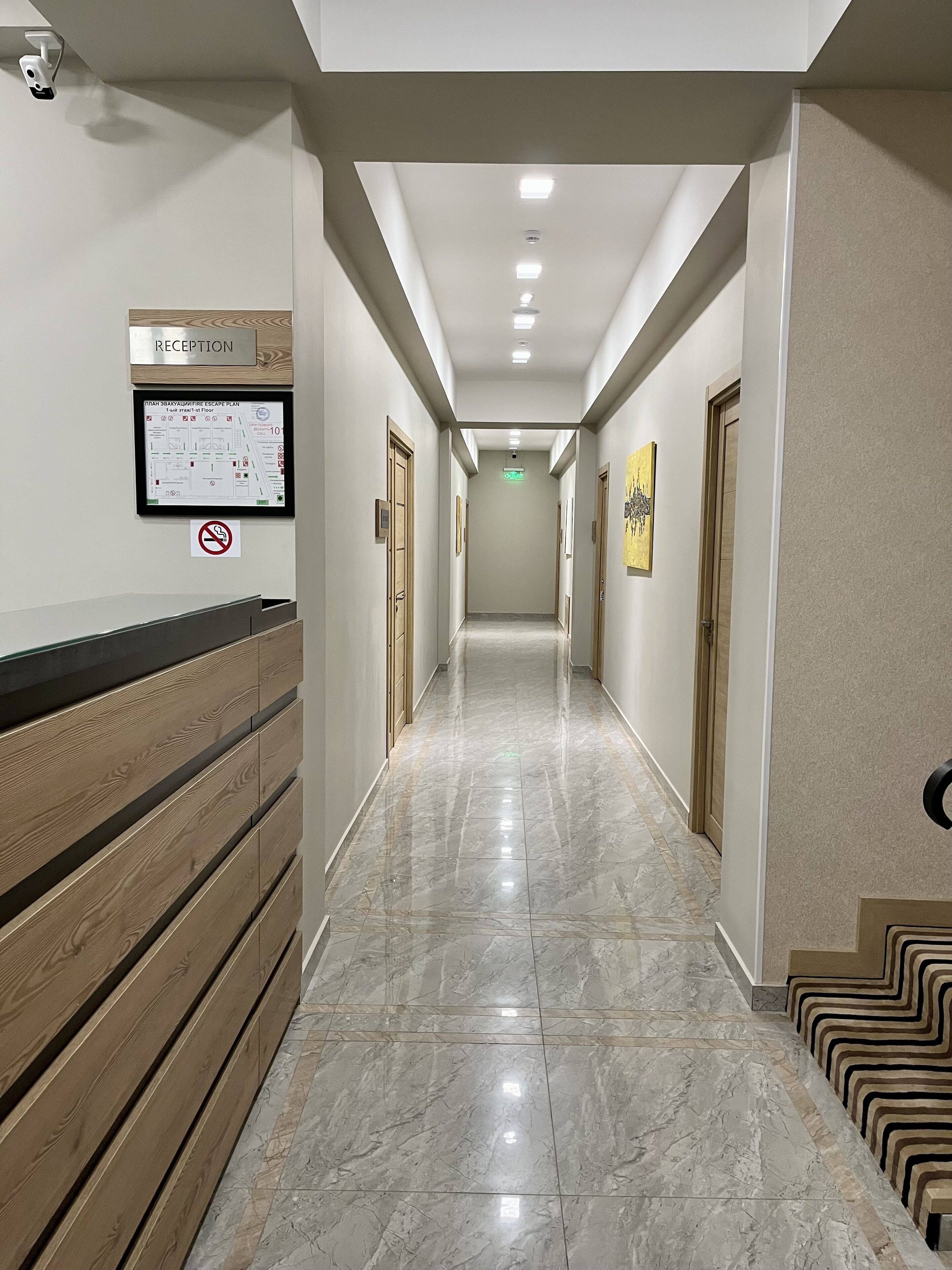 En hotellobby med en receptionsdisk, en skylt som visar var receptionen finns, en skylt som förbjuder rökning och en planritning på väggen.