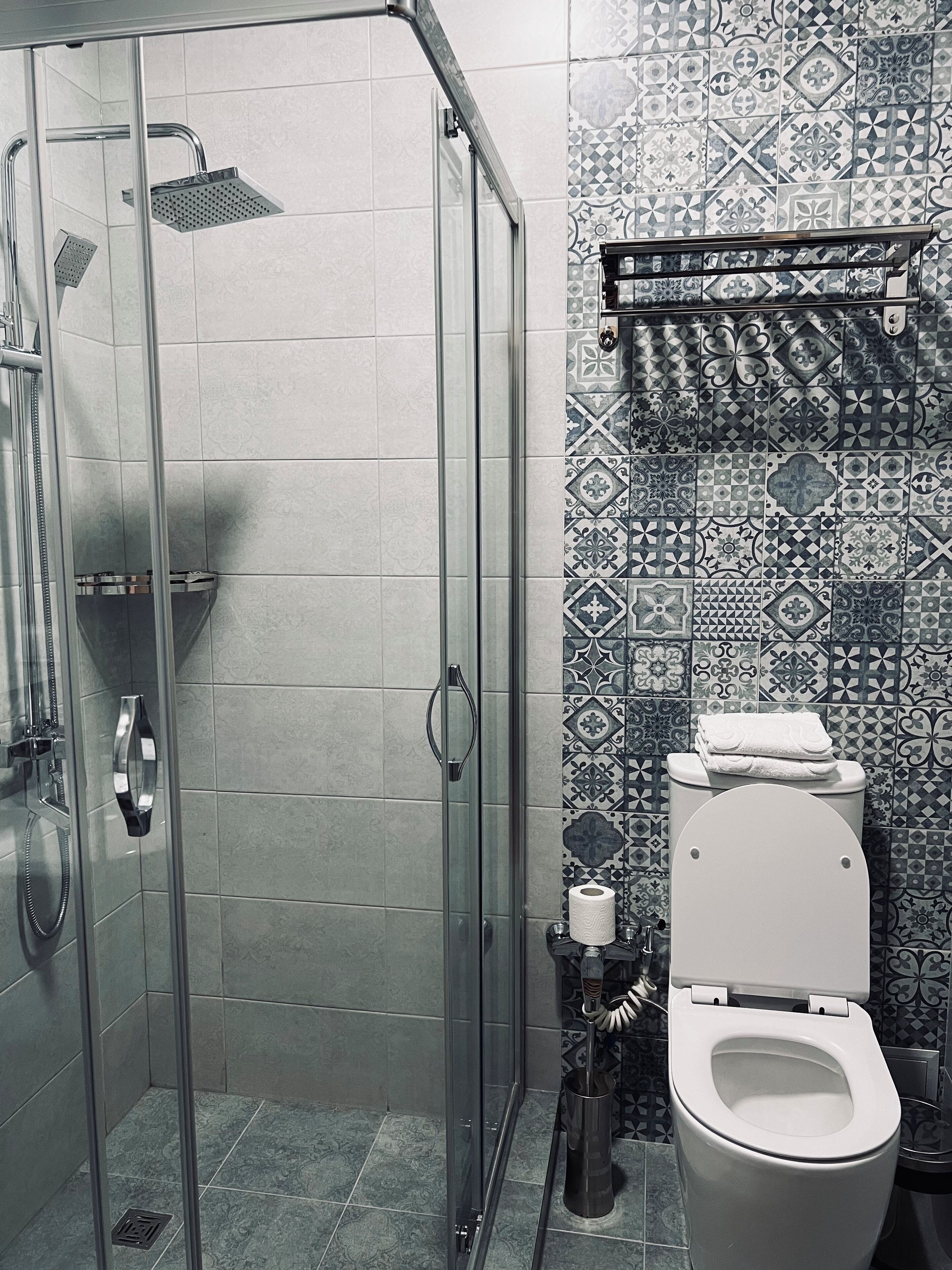 A bathroom with a glass-enclosed shower, a toilet, and patterned tiles on the walls.