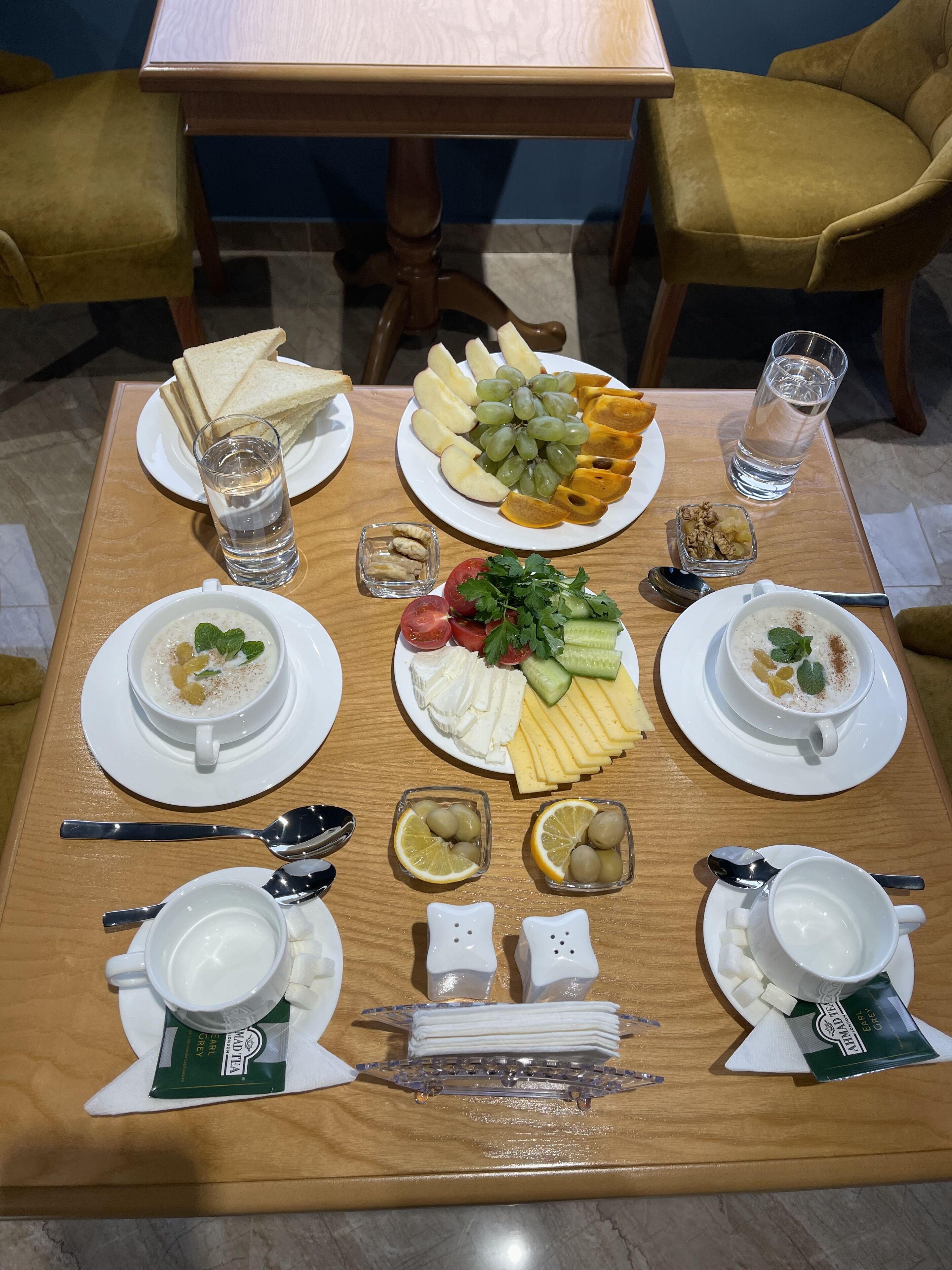 Una mesa de desayuno lista, con platos de comida, vasos de agua y sobres de té.