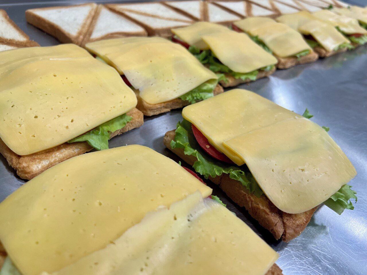 Sandwiches with cheese and lettuce on a metal surface.