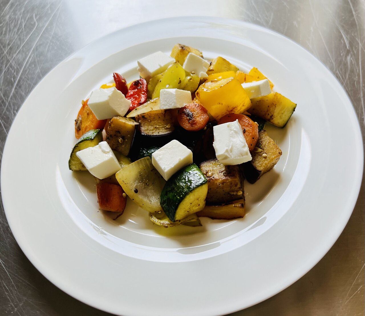 Une assiette blanche contenant des légumes rôtis et des cubes de fromage blanc.