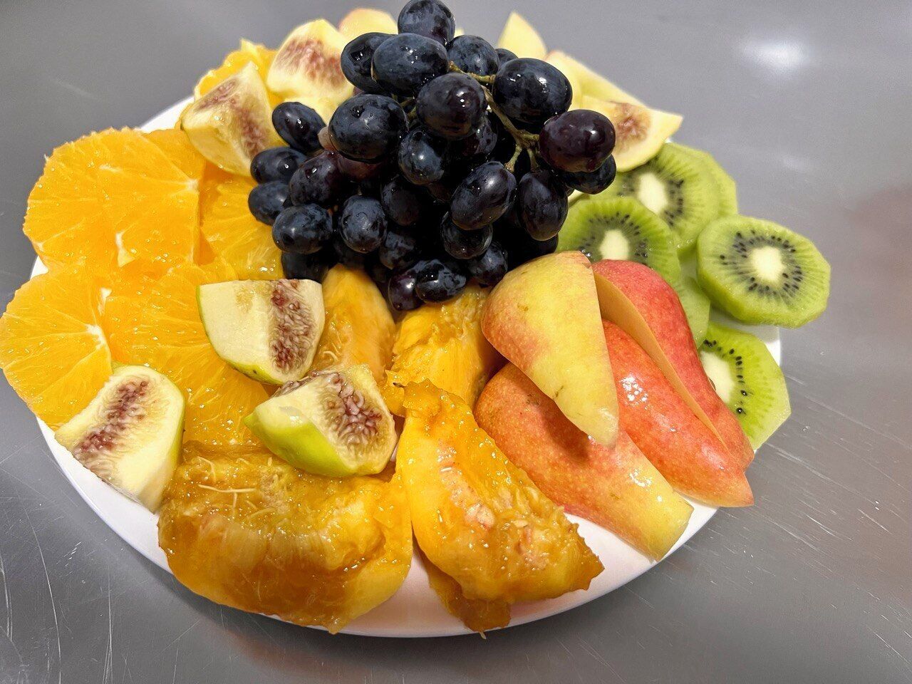Une assiette de fruits variés, notamment des raisins, des oranges, des kiwis et des pêches.