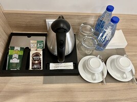 Bandeja de desayuno en una habitación de hotel con bolsitas de té, tetera, botellas de agua y tazas y platillos blancos.