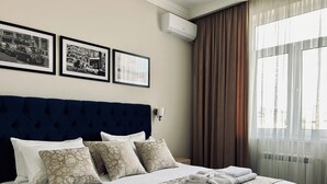 Una habitació d'hotel amb un llit gran, un panell de fons blau fosc i tres quadres penjats a la paret.