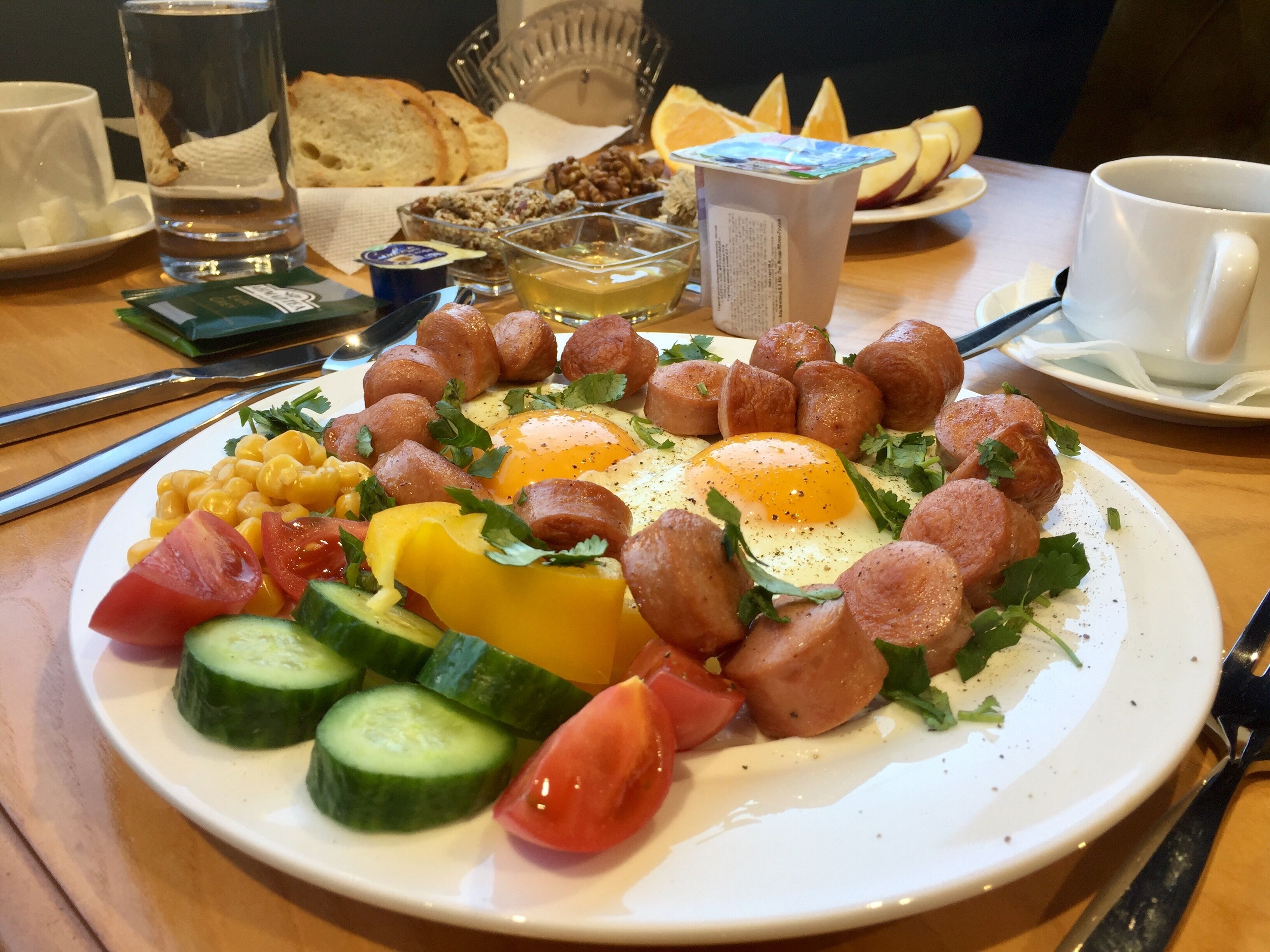 A breakfast plate with eggs, sausages, tomatoes, cucumbers, and cheese.