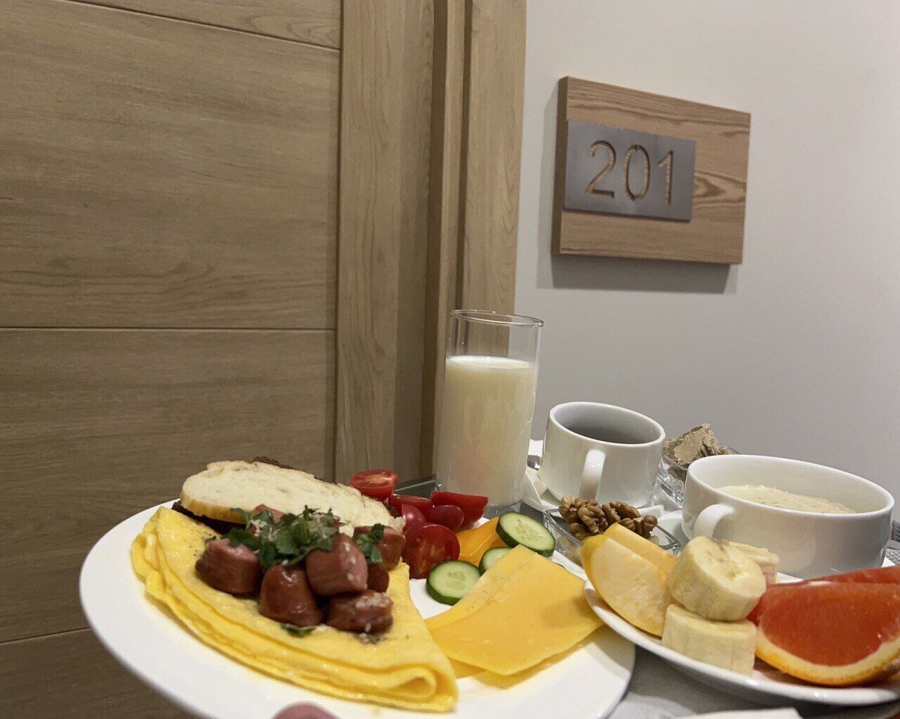 Uma mesa de café da manhã com um prato de ovos, queijo, tomates, pepinos e um copo de leite.