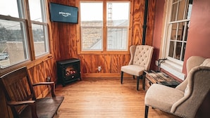 Ein gemütliches Zimmer mit Holzwänden, Kamin, Fernseher und großen Fenstern.