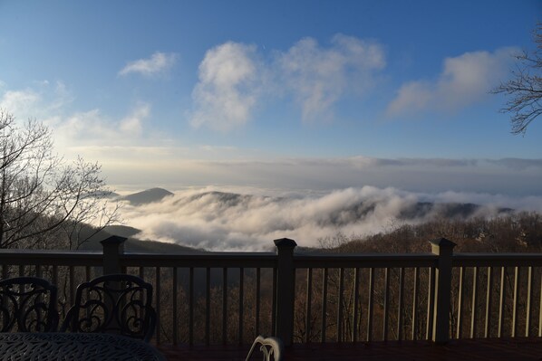 A deck with a railing overlooking a mountainous landscape with clouds below.