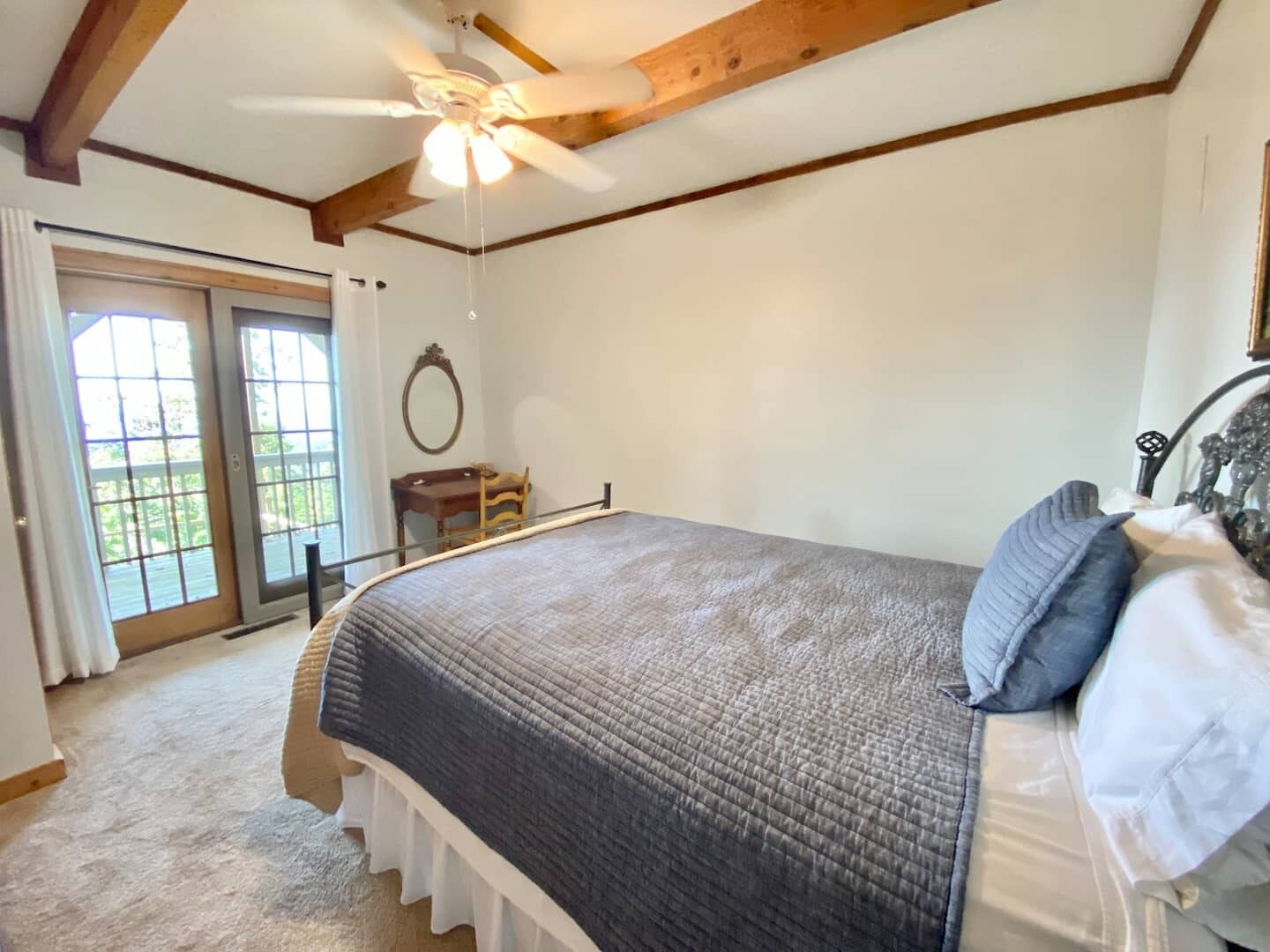 Une chambre avec un grand lit, un ventilateur de plafond et une vue sur l’extérieur, accessible par une porte-fenêtre coulissante.