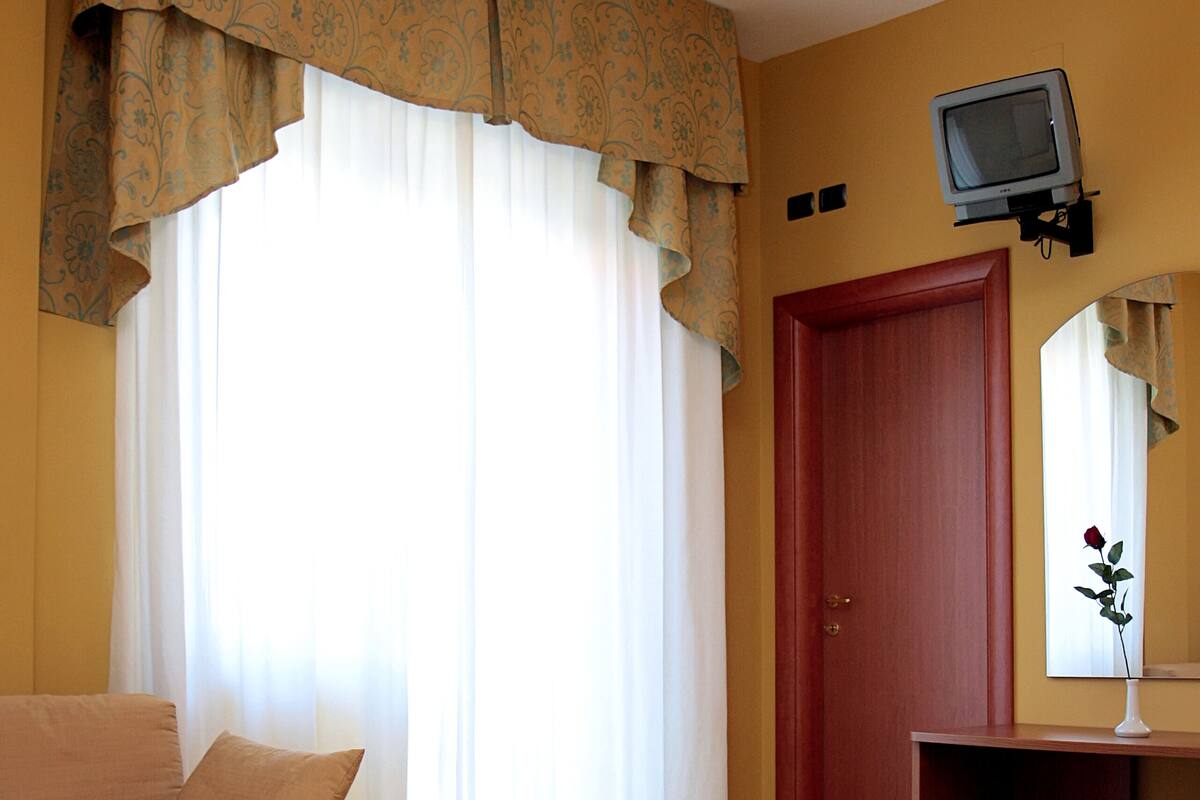 A hotel room with a bed, a sofa, a television mounted on the wall, and a window with curtains.