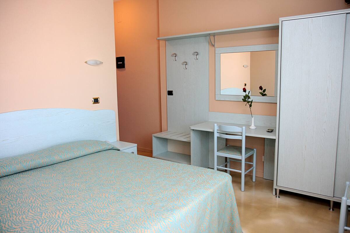 A bedroom with a bed, a desk, and a wardrobe.