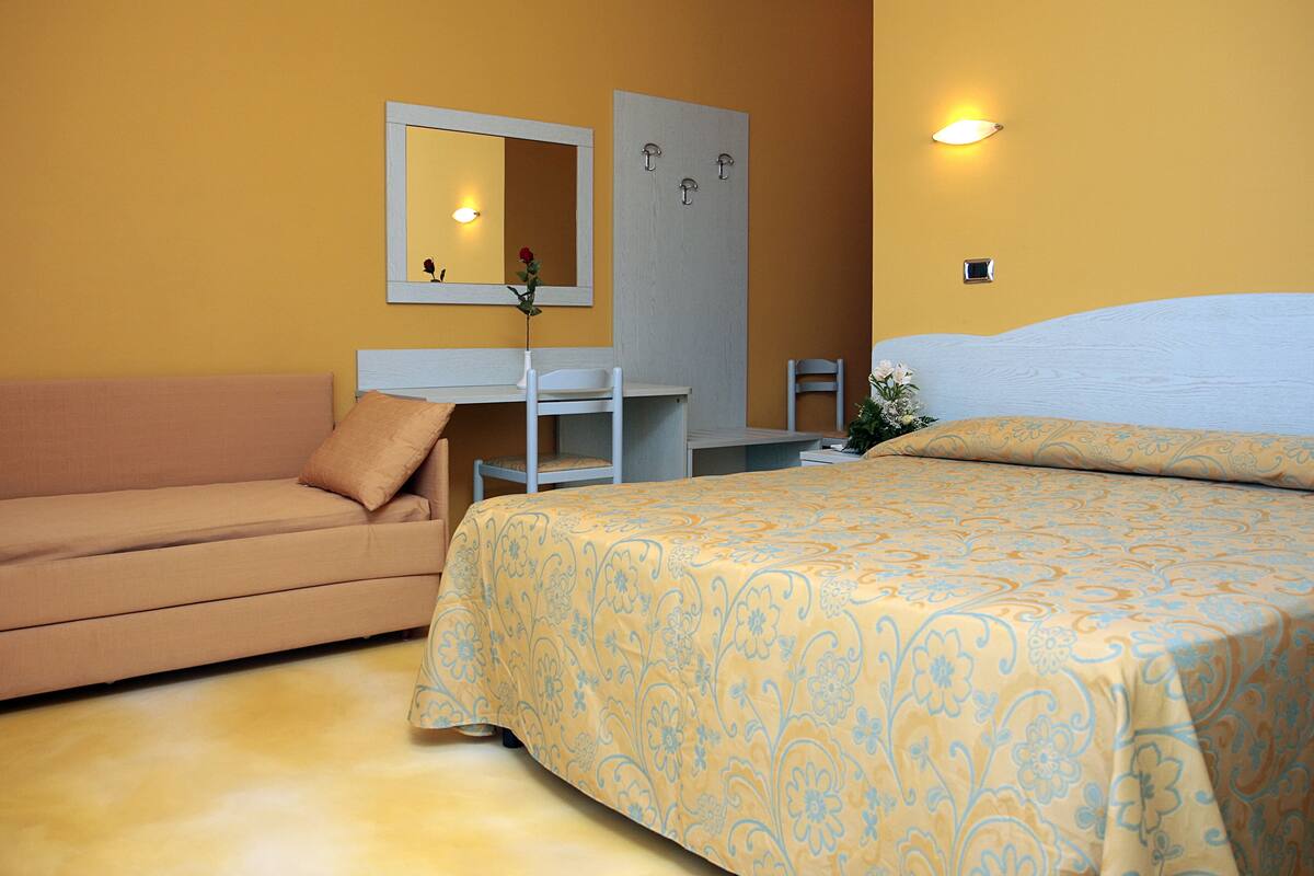 A hotel room with a bed, a sofa, a desk, and a mirror.