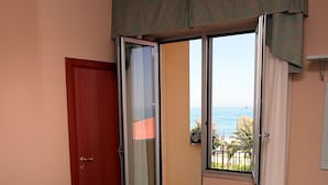 A bedroom with a bed, a door, a sliding glass door leading to a balcony, and a view of the sea.