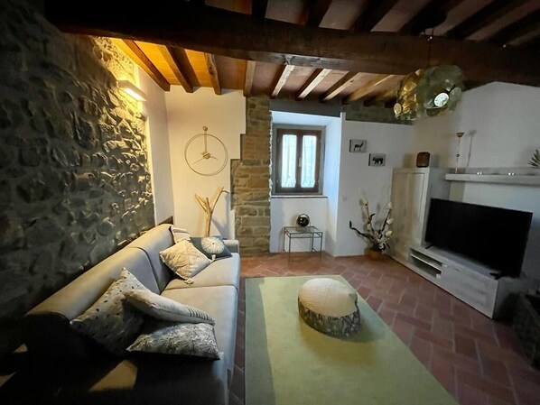 Un salon chaleureux avec un mur en pierre, un canapé agrémenté de coussins à motifs, un tapis vert, une cheminée et un téléviseur.
