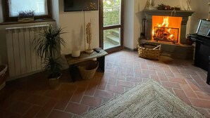 A cozy living room with a fireplace, a television, a window, and a potted plant. - Villa Borgo Soale in Tuscany—Reggello. Private pool and Wi-Fi (Toscana)