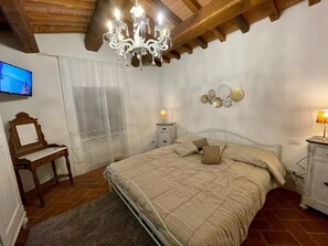 A bedroom with a bed, a wooden desk, a television, a chandelier, and decorative plates on the wall.