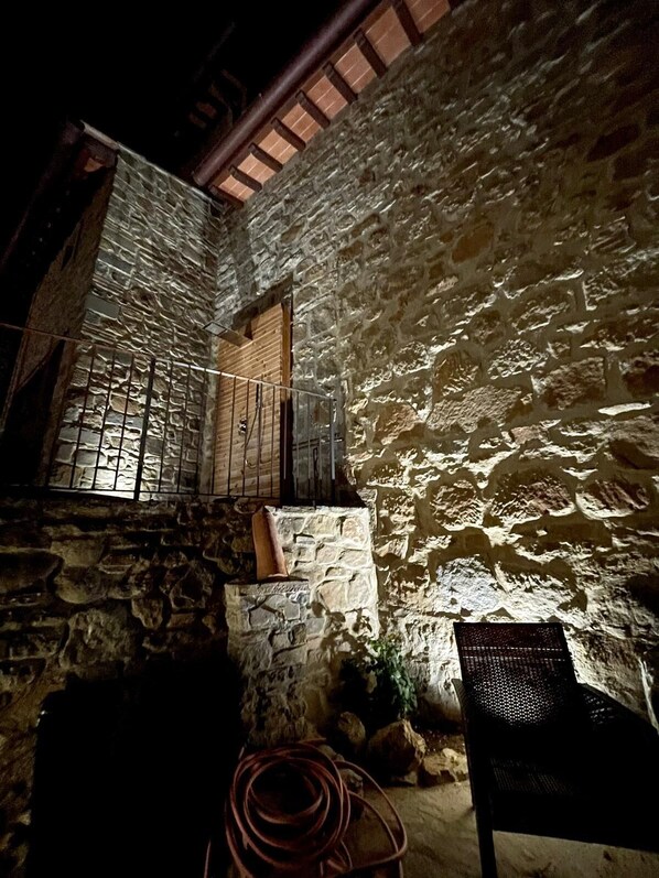 Un patio de piedra con una verja de metal, una puerta de madera y una silla.