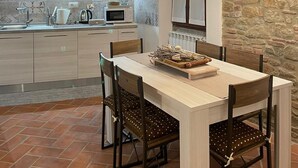 A modern kitchen with a stone accent wall, wooden ceiling beams, and a dining area with a rustic chandelier. - Villa Borgo Soale in Tuscany—Reggello. Private pool and Wi-Fi (Toscana)