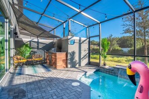 An indoor swimming pool with a glass enclosure, a wooden deck, and a lounge area with chairs.