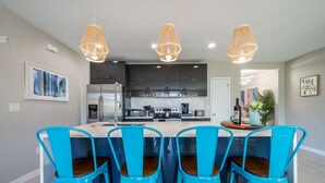 A modern kitchen with a central island, four blue chairs, and three hanging wicker pendant lights. - Disney-Themed Home with Pool and Game Room (Kissimmee)