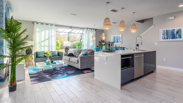 A modern kitchen with a central island, a dining area with a sofa, and a large window providing natural light. - Disney-Themed Home with Pool and Game Room (Kissimmee)