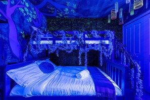 A bed with a headboard decorated with hanging plants, a dark textured wall behind, and a blue ambient light.