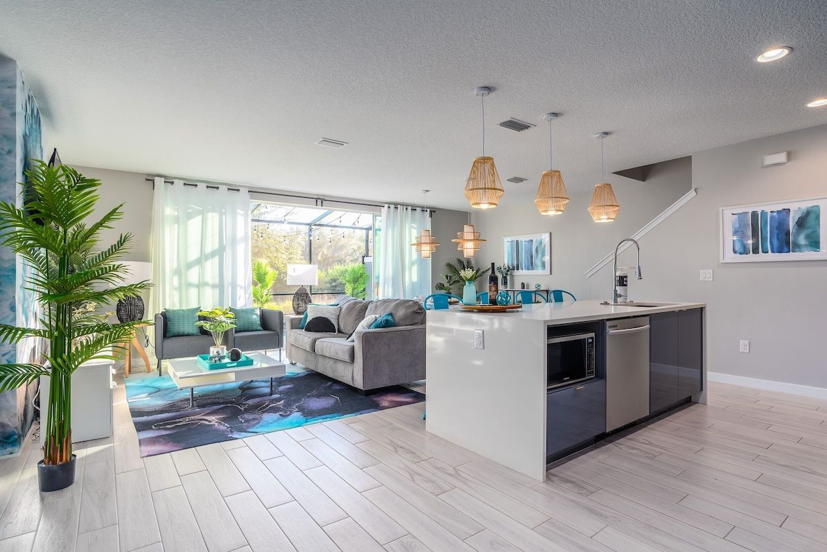 A modern kitchen with a central island, a dining area with a sofa and coffee table, and a staircase leading to an upper level.