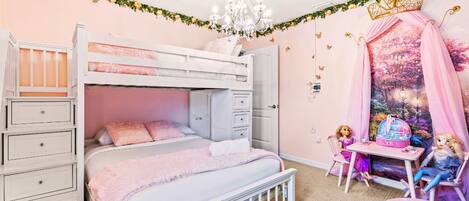 Un dormitorio con decoración rosa, que incluye una litera, un tocador y una mesa con muñecas.