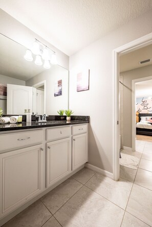 A modern bathroom with a large mirror, a sink with a black countertop, and a walk-in shower. - Sleeps 21 / Disney & Universal Retreat w/ Game Room + Pool, Spa (Kissimmee)