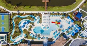 An aerial view of a resort with a swimming pool, a water slide, and a tennis court. - Sleeps 21 / Disney & Universal Retreat w/ Game Room + Pool, Spa (Kissimmee)